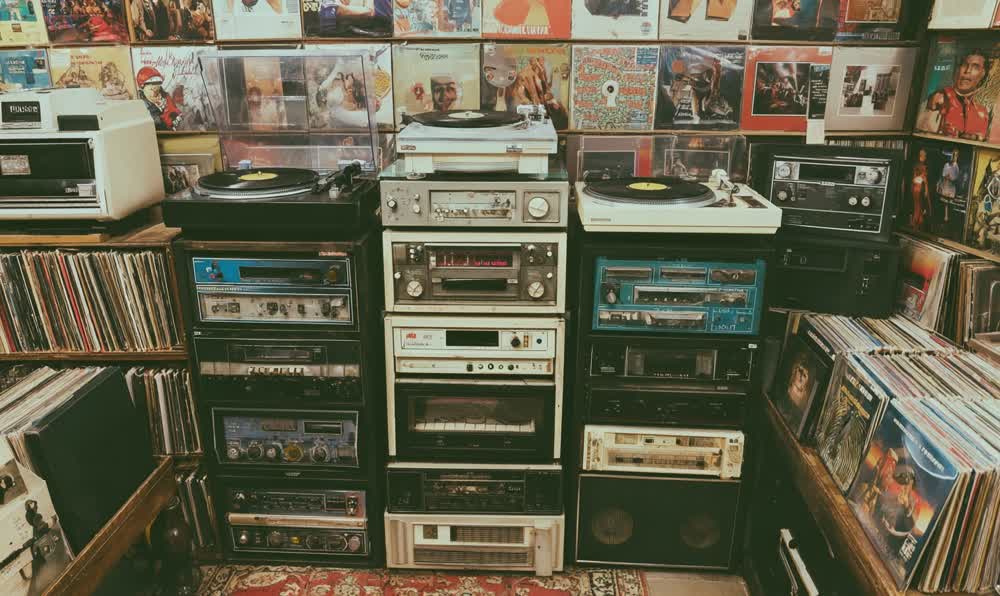 A retro record store listening station with headphones, album covers, posters, denim jacket, and warm shop lighting