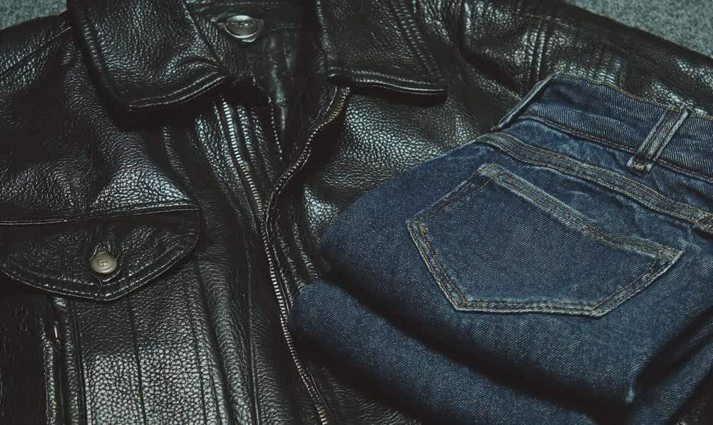 Black leather jacket and blue denim styled with retro sneakers, sunglasses, watch, cassette tapes, and night street lighting