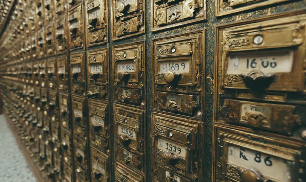 Wooden library card catalog drawers with typed cards, a book, warm reading room light, and a retro watch
