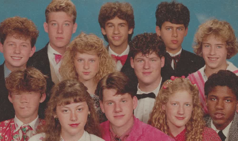 An 1980s school picture day setup with blue backdrop, flash camera, comb, and retro denim jacket