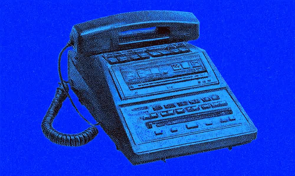 A vintage answering machine beside a corded telephone, cassette tape, notebook, and warm 1980s home decor