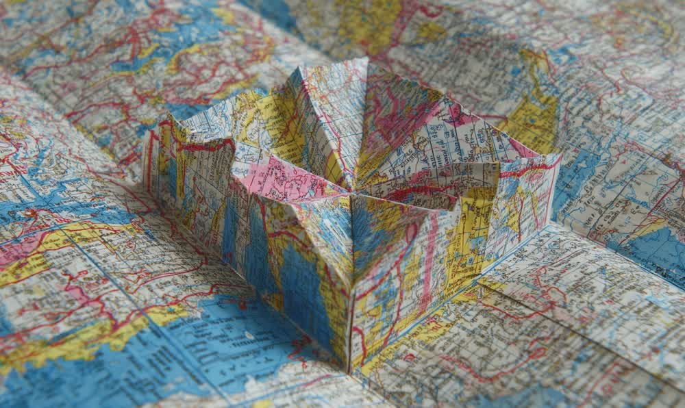 A colorful paper map being folded on a tabletop beside keys, sunglasses, and a retro leather jacket