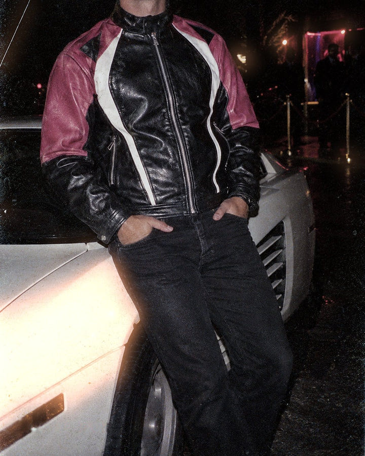 Pink Racer Jacket 1985 leaning on a white sports car at night