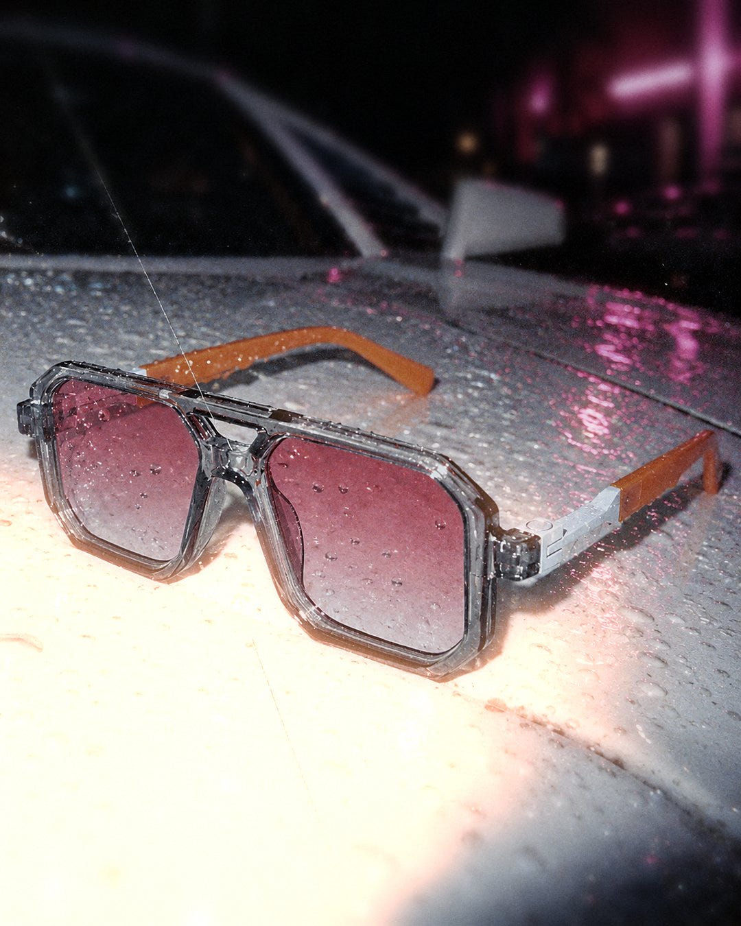 Pink Haze Sunglasses 1984 close up on a wet car hood at night