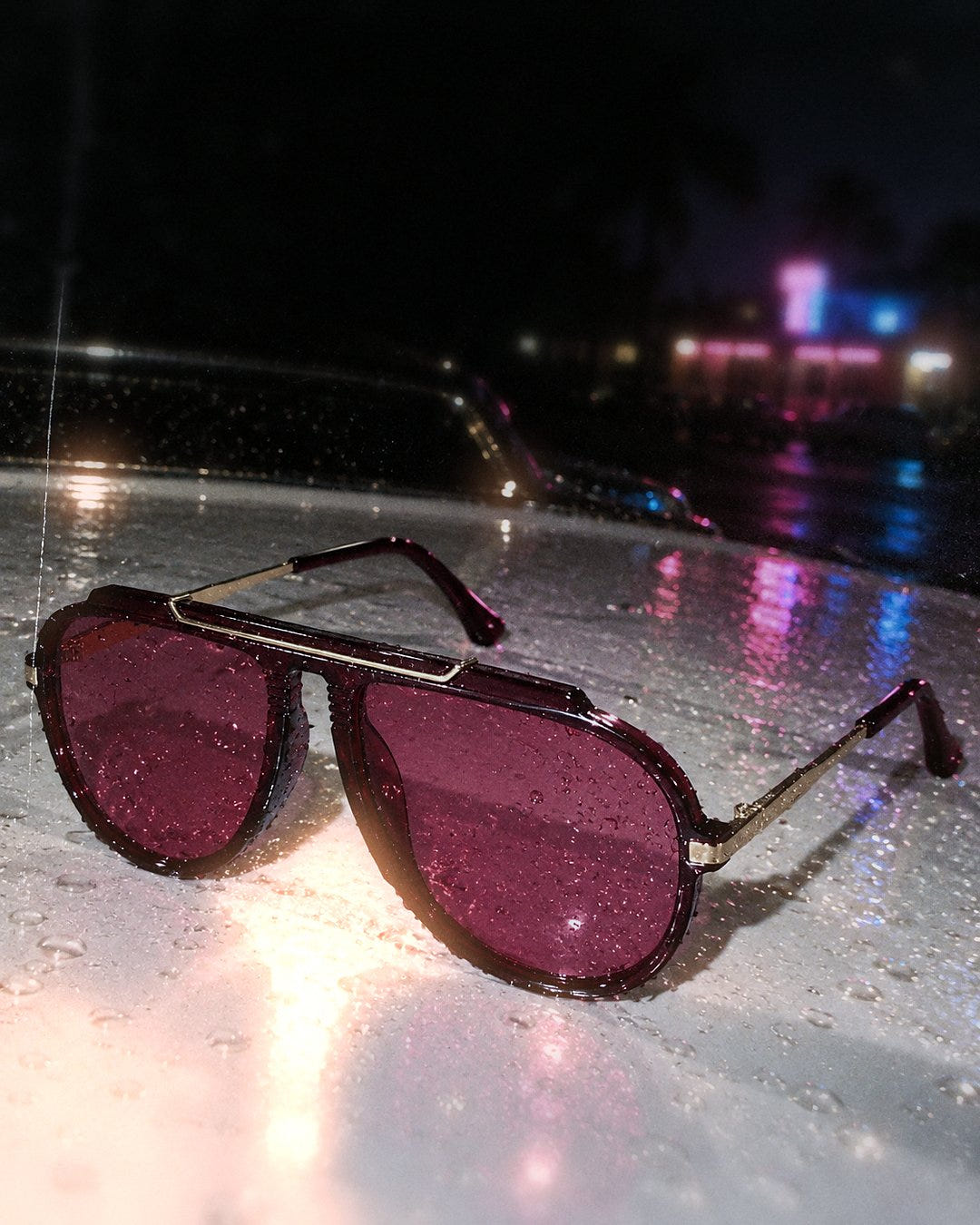 Magenta Pilot Sunglasses 1985 on a wet car hood at night