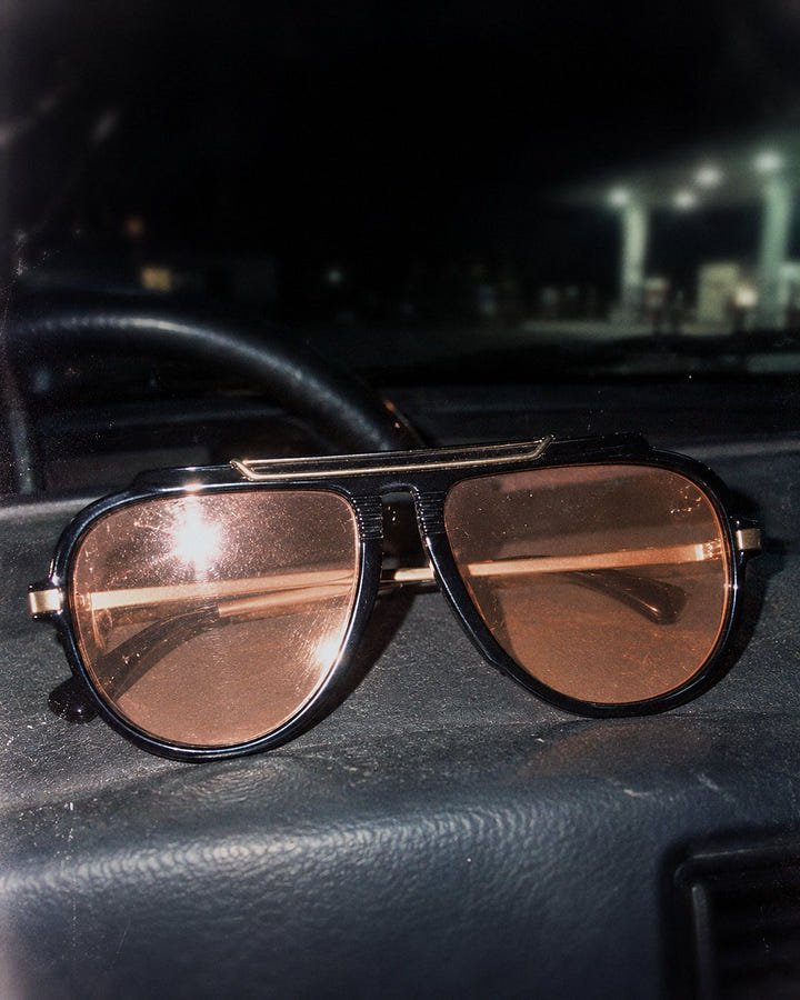 Magenta Pilot Sunglasses 1985 in black and light orange on a car dashboard at night